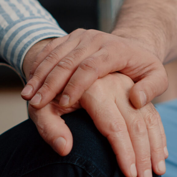 Close up of hands of senior patient and medical assistant at nursing facility. Nurse giving assistance to person sitting in wheelchair. Healthcare specialist showing support to disabled adult